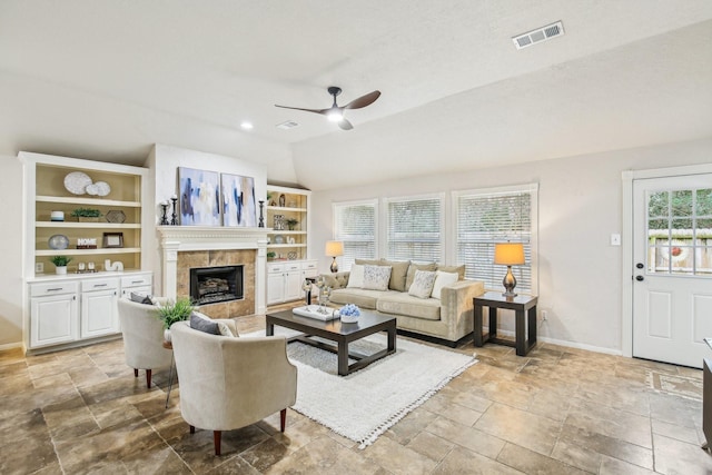 living room featuring built in shelves, ceiling fan, lofted ceiling, and a tile fireplace