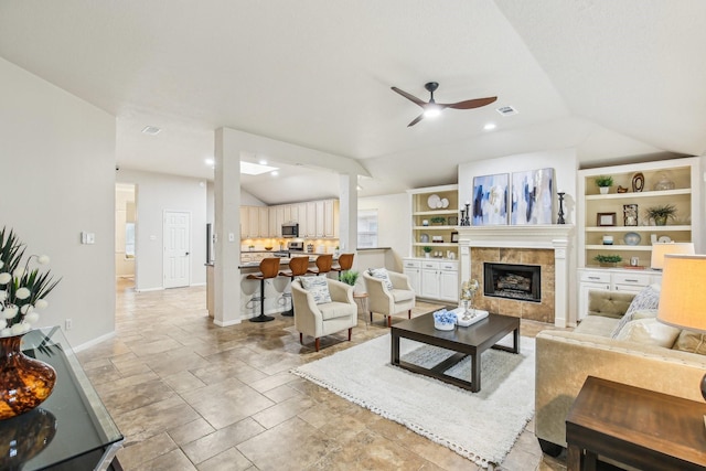 living room featuring a fireplace, built in shelves, vaulted ceiling, and ceiling fan