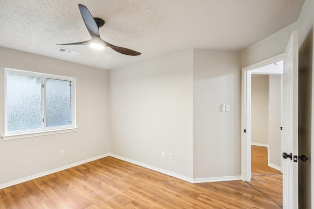 empty room featuring visible vents, baseboards, ceiling fan, light wood-type flooring, and a textured ceiling