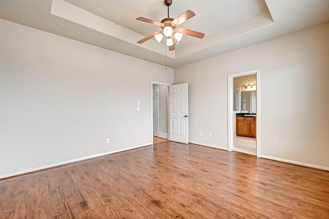 unfurnished bedroom featuring a tray ceiling, light hardwood / wood-style floors, ceiling fan, and ensuite bathroom