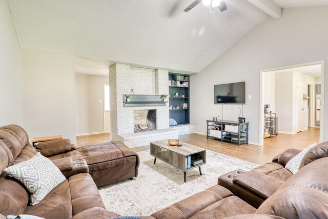 living room with lofted ceiling with beams, hardwood / wood-style flooring, ceiling fan, a brick fireplace, and built in shelves