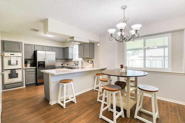 kitchen with double oven, hanging light fixtures, stainless steel refrigerator with ice dispenser, a notable chandelier, and kitchen peninsula