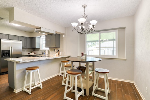 kitchen featuring decorative light fixtures, a textured ceiling, stainless steel fridge, gray cabinets, and kitchen peninsula