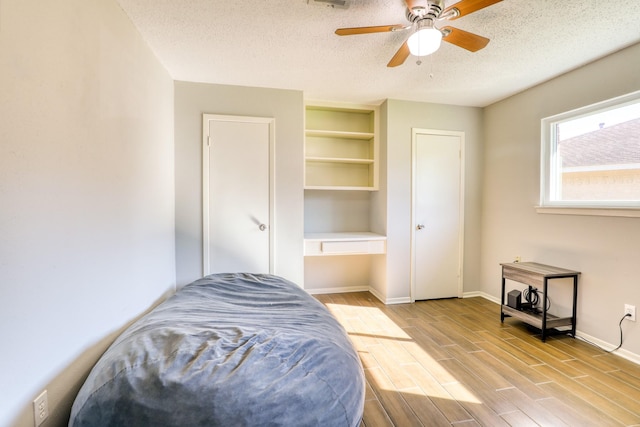 bedroom featuring ceiling fan, built in desk, a textured ceiling, and light wood-type flooring