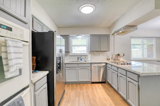 kitchen with appliances with stainless steel finishes, range hood, sink, backsplash, and kitchen peninsula