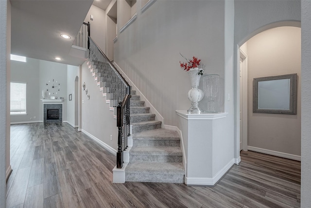 stairs with a tiled fireplace, hardwood / wood-style floors, and a towering ceiling