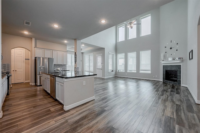 kitchen with white cabinetry, dark hardwood / wood-style floors, a tiled fireplace, and an island with sink