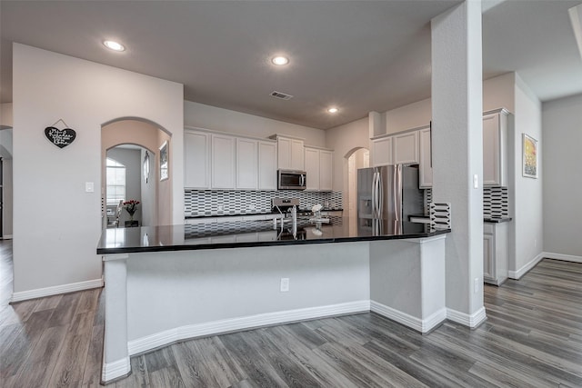 kitchen featuring tasteful backsplash, appliances with stainless steel finishes, kitchen peninsula, hardwood / wood-style flooring, and white cabinets