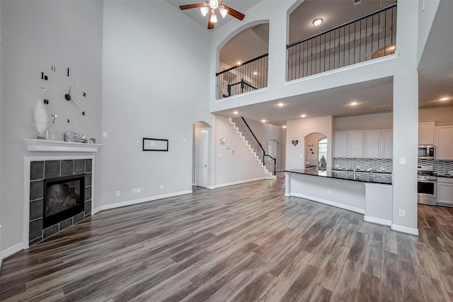 unfurnished living room featuring a towering ceiling, wood-type flooring, a tile fireplace, and ceiling fan