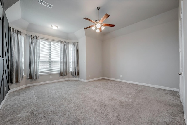 unfurnished room with a raised ceiling, vaulted ceiling, light colored carpet, and ceiling fan