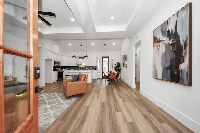 living room with a raised ceiling, ceiling fan, and light hardwood / wood-style flooring