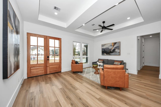 living room featuring french doors, ceiling fan, a raised ceiling, and light wood-type flooring