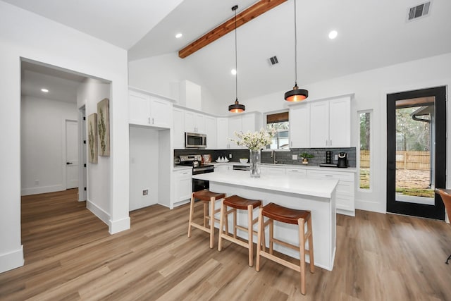 kitchen featuring appliances with stainless steel finishes, white cabinetry, backsplash, hanging light fixtures, and a kitchen island with sink