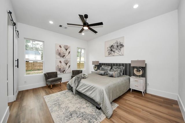 bedroom featuring hardwood / wood-style flooring, ceiling fan, a barn door, and multiple windows