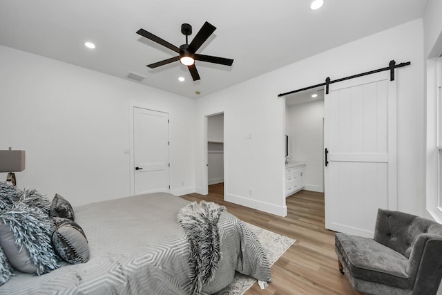 bedroom featuring ceiling fan, ensuite bathroom, a barn door, a closet, and light wood-type flooring