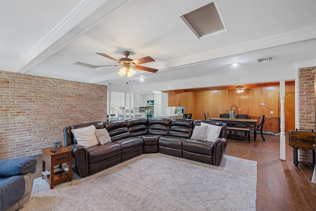 living room featuring beamed ceiling, ceiling fan, brick wall, and dark wood-type flooring