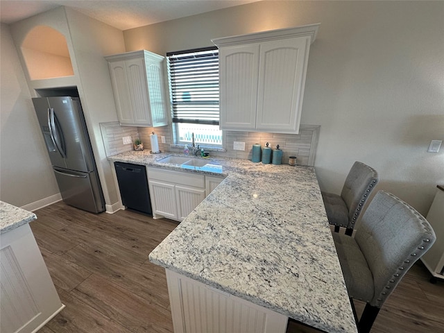 kitchen featuring white cabinetry, black dishwasher, a breakfast bar area, stainless steel fridge, and light stone countertops