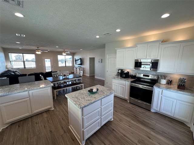 kitchen featuring appliances with stainless steel finishes, dark hardwood / wood-style floors, white cabinets, a center island, and light stone counters