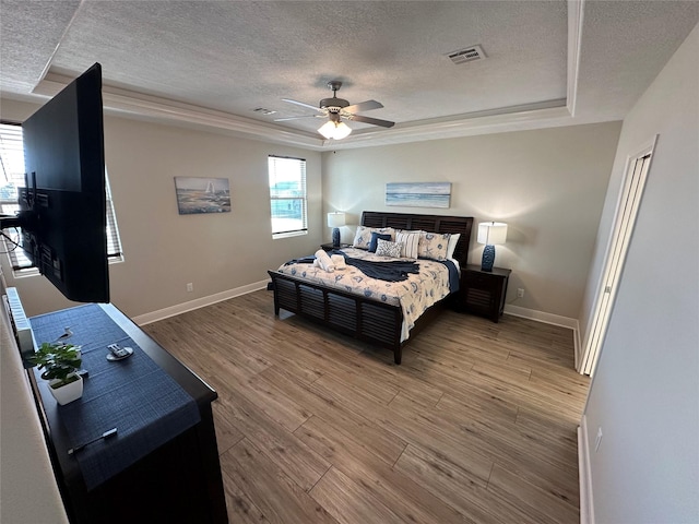 bedroom with ceiling fan, a raised ceiling, hardwood / wood-style floors, and a textured ceiling