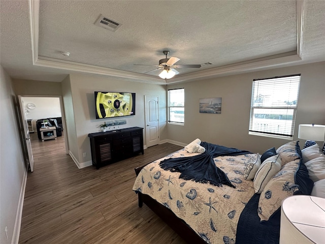 bedroom featuring dark hardwood / wood-style flooring, ornamental molding, ceiling fan, a tray ceiling, and a textured ceiling