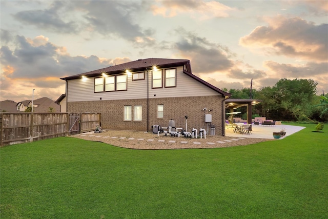 back house at dusk featuring a lawn and a patio