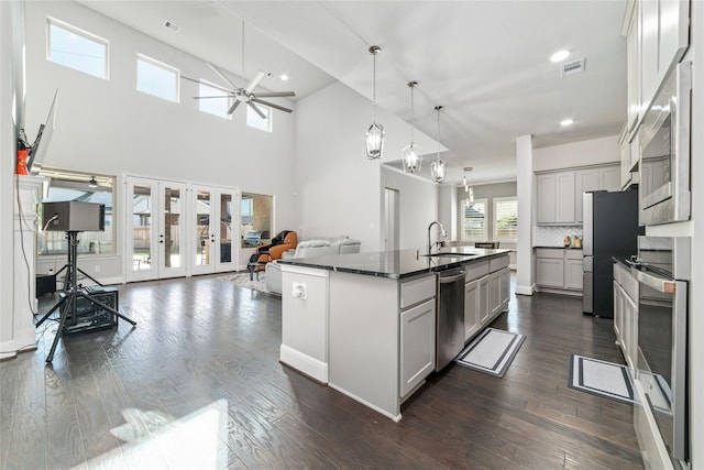 kitchen with sink, hanging light fixtures, appliances with stainless steel finishes, a kitchen island with sink, and backsplash