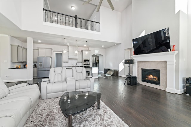 living room with a tiled fireplace, a towering ceiling, and dark hardwood / wood-style flooring