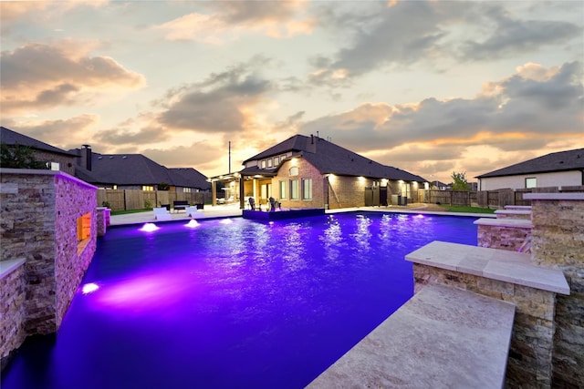 pool at dusk featuring pool water feature and a patio area