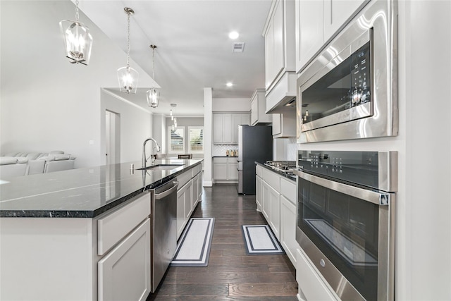 kitchen with sink, appliances with stainless steel finishes, white cabinetry, a center island with sink, and decorative light fixtures