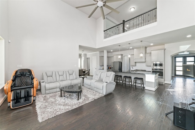 living room featuring dark wood-type flooring, sink, ceiling fan, and a towering ceiling