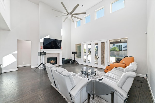 living room with dark hardwood / wood-style flooring, ceiling fan, a high ceiling, a tiled fireplace, and french doors