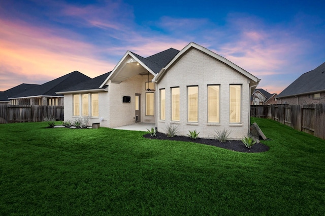 back house at dusk with a patio and a lawn