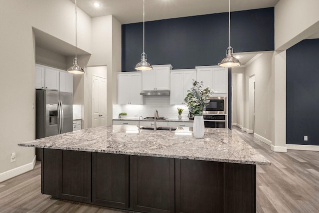 kitchen featuring a towering ceiling, decorative light fixtures, white cabinets, stainless steel appliances, and a spacious island