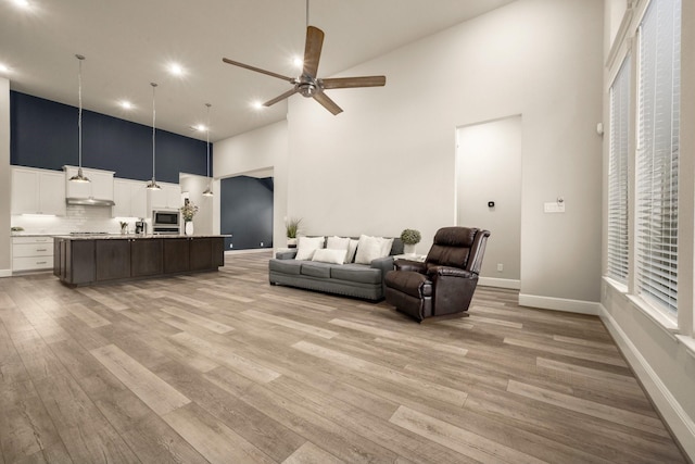 living room featuring a high ceiling, ceiling fan, and light hardwood / wood-style floors