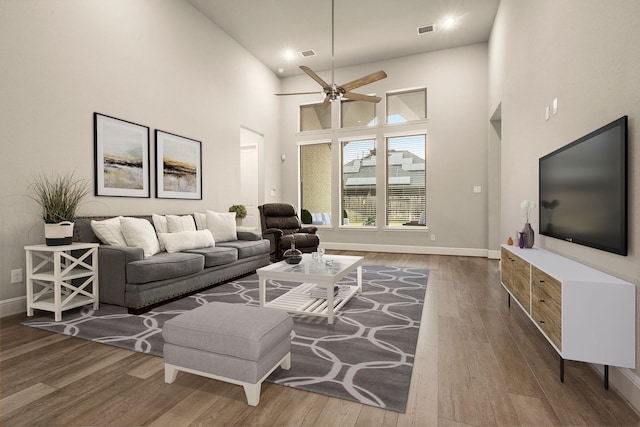 living room featuring wood-type flooring, a towering ceiling, and ceiling fan