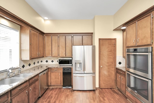 kitchen featuring stainless steel appliances, tasteful backsplash, sink, and light stone counters