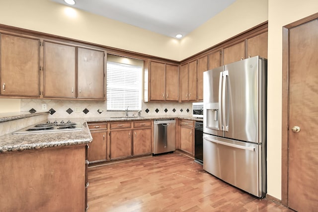 kitchen with stainless steel appliances, sink, decorative backsplash, and light wood-type flooring