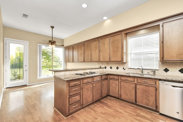 kitchen with dishwashing machine, sink, light stone counters, decorative backsplash, and kitchen peninsula