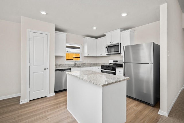 kitchen with sink, white cabinetry, stainless steel appliances, a center island, and light stone counters