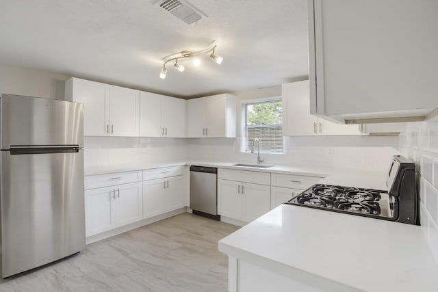 kitchen with appliances with stainless steel finishes, white cabinetry, sink, backsplash, and a textured ceiling