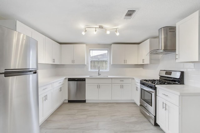 kitchen featuring appliances with stainless steel finishes, tasteful backsplash, sink, white cabinets, and wall chimney range hood