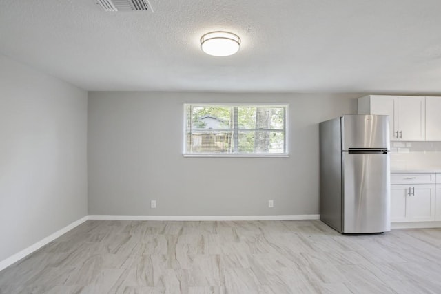 kitchen with stainless steel refrigerator, white cabinetry, and a textured ceiling