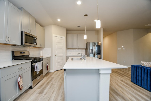 kitchen featuring sink, hanging light fixtures, light hardwood / wood-style flooring, an island with sink, and stainless steel appliances