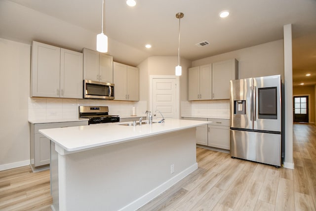 kitchen with sink, light hardwood / wood-style flooring, pendant lighting, stainless steel appliances, and a kitchen island with sink