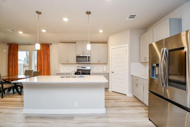 kitchen with white cabinetry, a center island with sink, pendant lighting, stainless steel appliances, and decorative backsplash