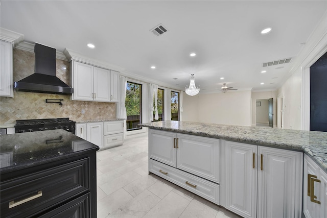 kitchen featuring light stone countertops, wall chimney range hood, white cabinets, and range