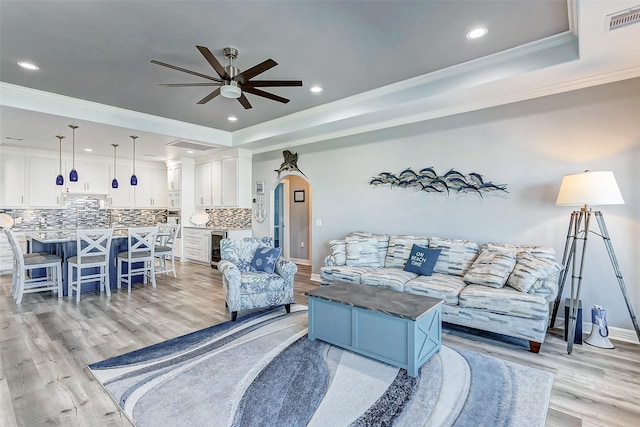 living room featuring crown molding, ceiling fan, a tray ceiling, and light wood-type flooring