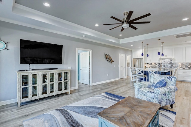 living room with crown molding, a raised ceiling, and light hardwood / wood-style flooring