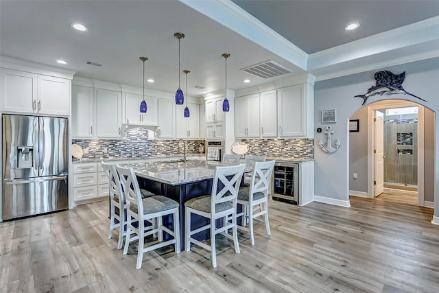 kitchen with white cabinetry, an island with sink, wine cooler, stainless steel appliances, and light stone countertops