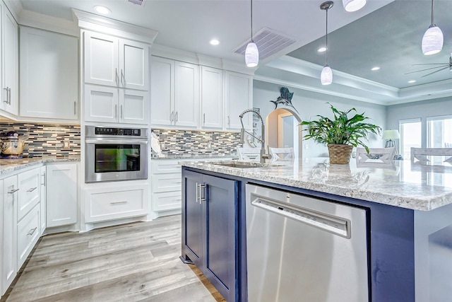 kitchen featuring sink, appliances with stainless steel finishes, white cabinetry, an island with sink, and a raised ceiling